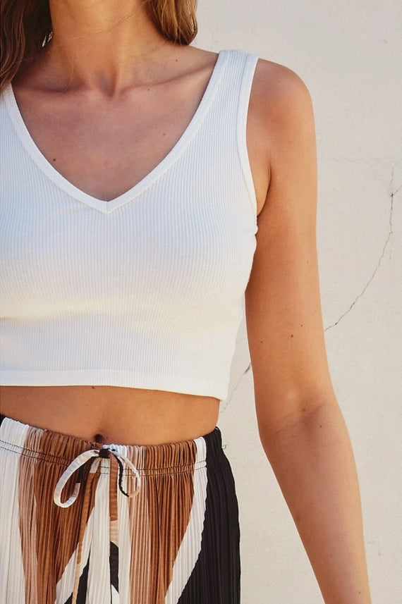 Person wearing a white tank top and patterned pants against a neutral background