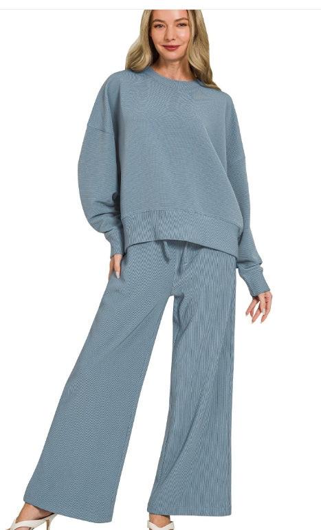 Model wearing a blue ribbed sweater and pants set on a white background