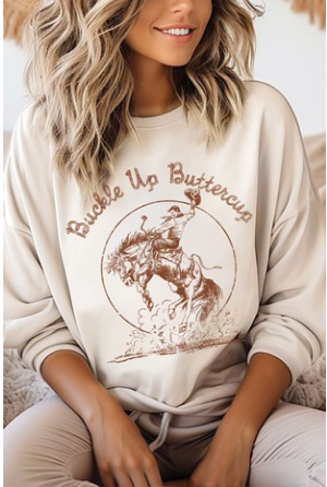 Model wearing a beige brushed sweatshirt with the text 'BUCKLE UP BUTTERCUP' printed on the front.