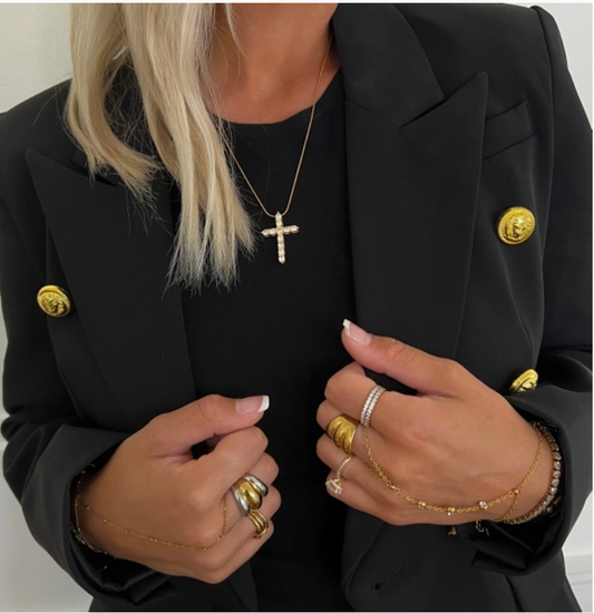Model wearing a gold-colored necklaces, including a diamond cross necklace, and gold-colored rings.