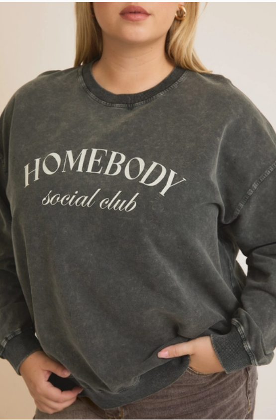 A woman wearing a gray sweatshirt with the text 'HOMEBODY SOCIAL CLUB' printed on the front.