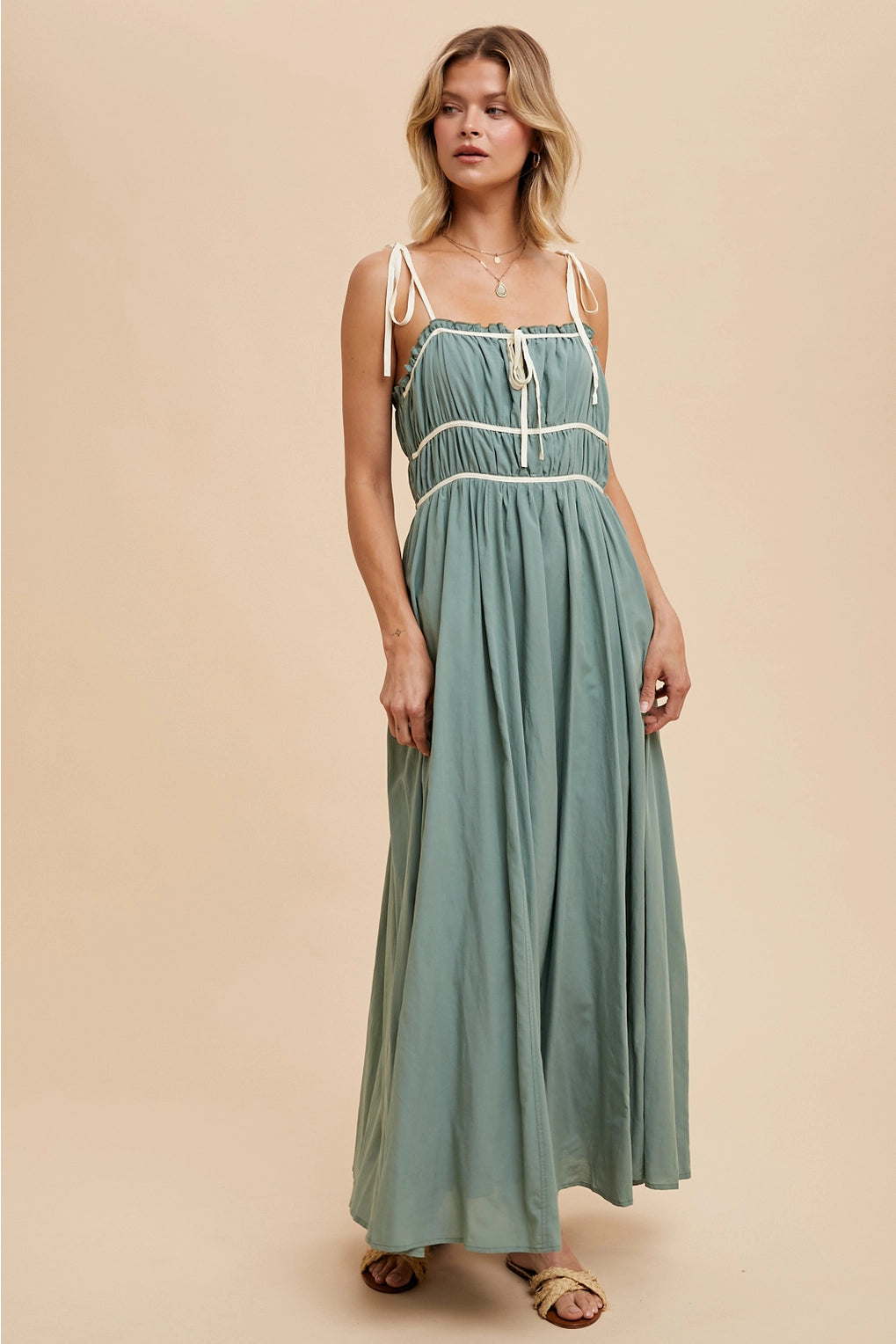 Model wearing a long green dress with pockets against a beige background
