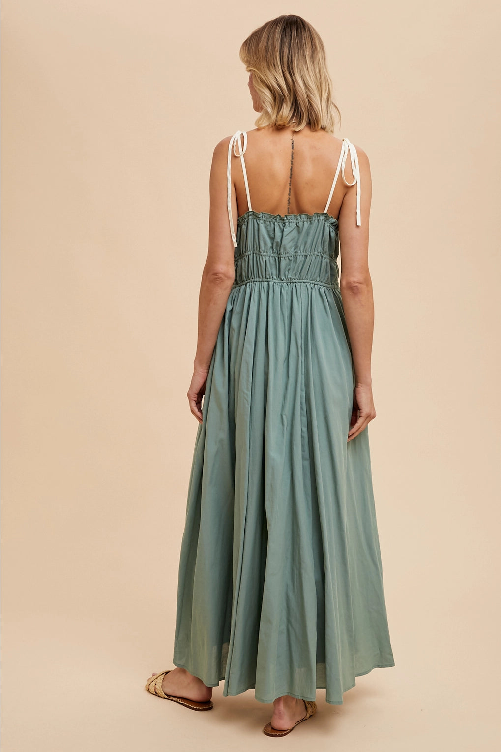 Back of model wearing a long green dress with pockets against a beige background
