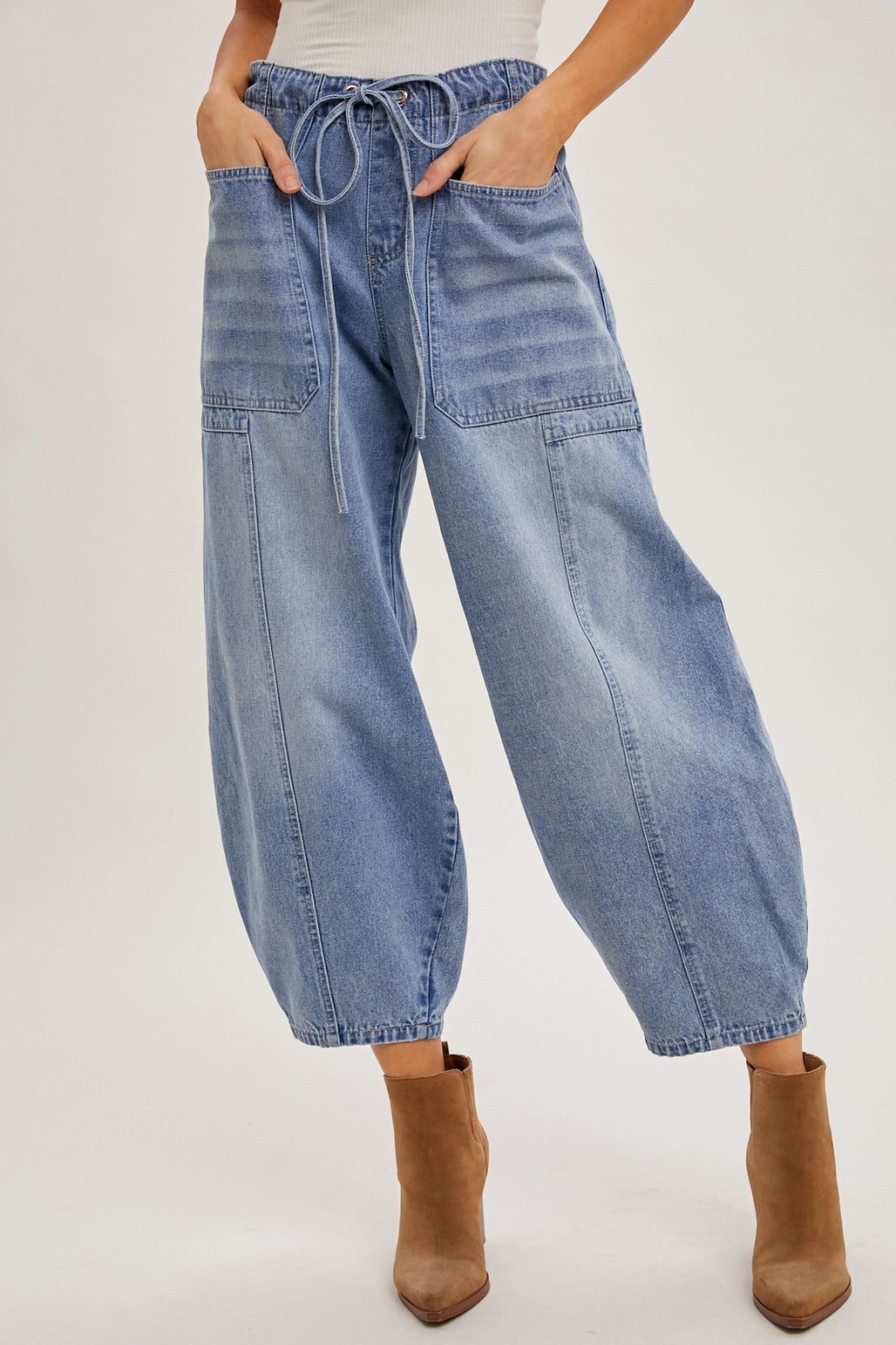A pair of mid-waist denim barrel jeans with an adjustable drawstring, in a light wash. 